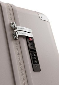 Lichtbeige harde koffer met dubbele zilveren ritsen en een zwart cijferslot. Geperforeerd oppervlak met logo-accenten.