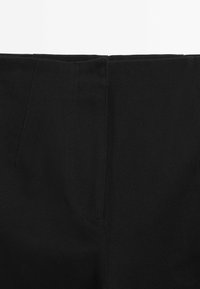 Gros plan sur un tissu noir avec une texture de tissage en diagonale visible et une couture verticale subtile au centre.