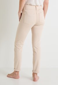 Jeans ajustados beige de cintura alta, con puños enrollados y bolsillos parche en la parte trasera. Textura de tela de mezcla de algodón suave.