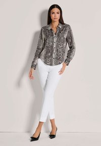 Langärmliges Hemd mit einem Schwarz-Weiß-Schlangendruck, mit Knöpfen und einem Kragen, kombiniert mit enger weißen Hose und schwarzen spitzen Schuhen.