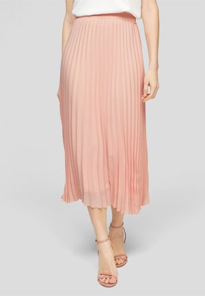 Jupe midi plissée en tissu rose doux, dotée d'une taille ajustée et d'un design fluide. Accompagnée de sandales à lanières assorties.