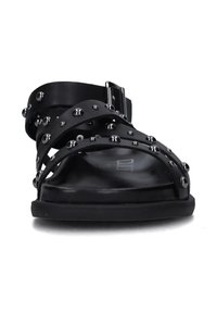 Sandali neri con cinturini, caratterizzati da borchie metalliche, suola piatta e fibbia alla caviglia. Texture liscia con un design minimalista.