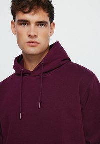 Felpa viola con cordini, realizzata in un tessuto morbido. Presenta una tasca a canguro e polsini a coste, offrendo un design dal taglio rilassato.