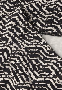 Černobílá látka s vzorovaným motivem a texturovaným povrchem; nepravidelný, abstraktní design; měkký, elastický textil; viditelné surové okraje.