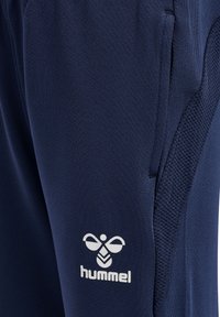 Marina atletiska byxor i strukturerad tyg med en vit Hummel-logotyp. Inkluderar sidofickor och en slät midjeband.