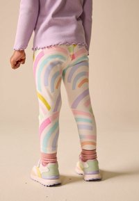 Legingi ar krāsainu varavīksnes rakstu pasteļtoņos, izgatavoti no ribotas auduma. Kombinēti ar sportiskām kedām gaišās krāsās.