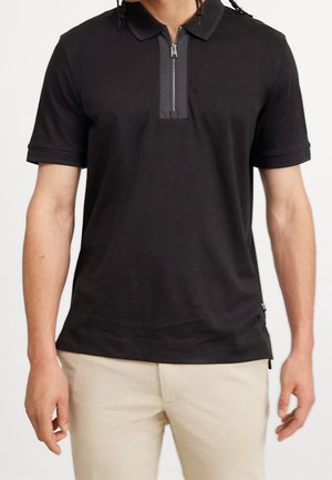 Black polo shirt with a zippered collar, featuring short sleeves and a textured fabric. Accents include a contrasting panel at the neck.