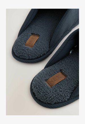 Mørkeblå slippers med en tekstureret overdel, blød fleeceforing og et brunt lædermærke. Afrundet form med polstrede indlægssåler for komfort.