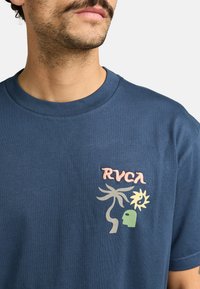 Camiseta de algodón color azul marino con cuello redondo, que presenta el texto bordado "RVCA" en rosa y diseños gráficos de una palmera y un sol en colores pastel.