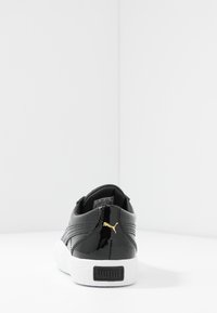 Sneaker in pelle patinata nera con suola in gomma bianca testurizzata, accento del logo dorato e dettagli di cucitura sottili. Design alto.