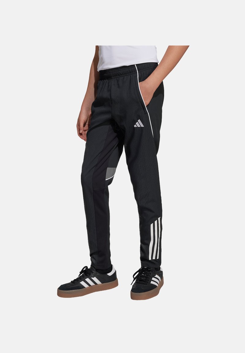 Schwarze Sporthose mit elastischem Bund, weißen Streifen an den Beinen und einem geometrischen Muster an der Seite, getragen mit schwarzen Schuhen.