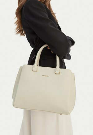 Donna che tiene una grande borsa color crema Gino Rossi con doppi manici, indossando una maglia nera a maniche lunghe e una gonna chiara.