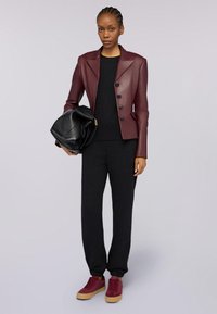 Blazer in pelle fitted bordeaux con due bottoni, top nero a maniche lunghe, pantaloni neri affusolati e sneakers bordeaux con suola beige.