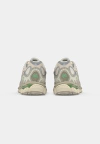 Baskets de sport avec une tige en maille et en caoutchouc, présentant des accents beige, gris et vert, ainsi qu'un système de amorti en gel visible.
