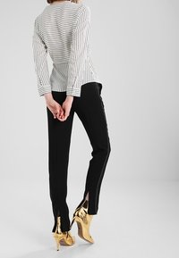 Gestreiftes weißes und schwarzes Langarmoberteil, kombiniert mit schwarzen Hosen mit seitlichen Schlitzen und glänzenden goldenen Stilettos.