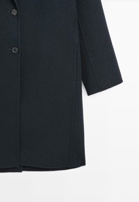 Cappotto di lana blu navy con taglio dritto, davanti a un solo petto e tre bottoni. Tessuto strutturato con grandi tasche laterali.