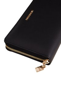 Portafoglio in pelle nera con cerniera e dettagli in oro, caratterizzato da una texture liscia e un logo metallizzato. Il cursore della cerniera include un dettaglio a forma di charm.