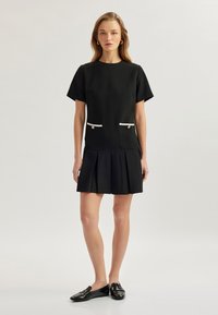 Vestido negro con mangas cortas, acentos de bolsillo blancos y falda plisada. Hecho de tela texturizada. Combinado con mocasines negros.