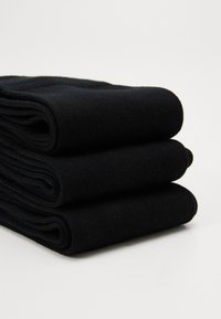 Crne pamučne čarape složene tri visine, s rebrastom teksturom i zaobljenim rubovima. Čini se da je materijal mekan i fleksibilan.