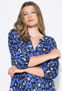 Abito in stampa leopardata blu realizzato in tessuto leggero, con scollo a V, maniche a tre quarti e dettagli con bottoni lungo la parte frontale.