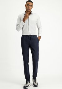 Camisa blanca de botones con una textura sutil, combinada con pantalones de cintura elástica en color marino y zapatillas grises y negras. Diseño simple y limpio.