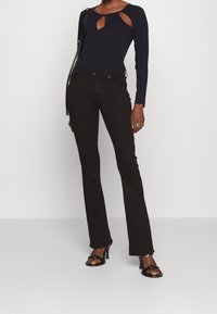 Långärmad svart bodysuit med nyckelhålsutsnitt, kombinerad med svarta tajta jeans och klacksandaler med remmar, vilket skapar en elegant silhuett.