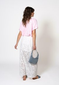 Rosa t-skjorte med korte ermer, kombinert med et langt skjørt av hvit blonde og en blå denimveske. Flate sandaler fullfører antrekket.