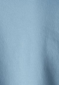 Tessuto blu chiaro con una superficie liscia, che mostra un colore uniforme e una finitura opaca e morbida. Nessun motivo o hardware visibile.