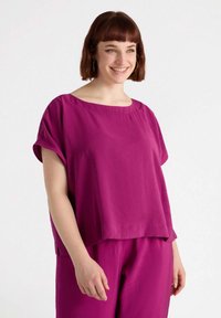Top oversized fucsia con maniche corte, scollatura rotonda e orlo appena sopra la vita. Texture liscia con vestibilità comoda.