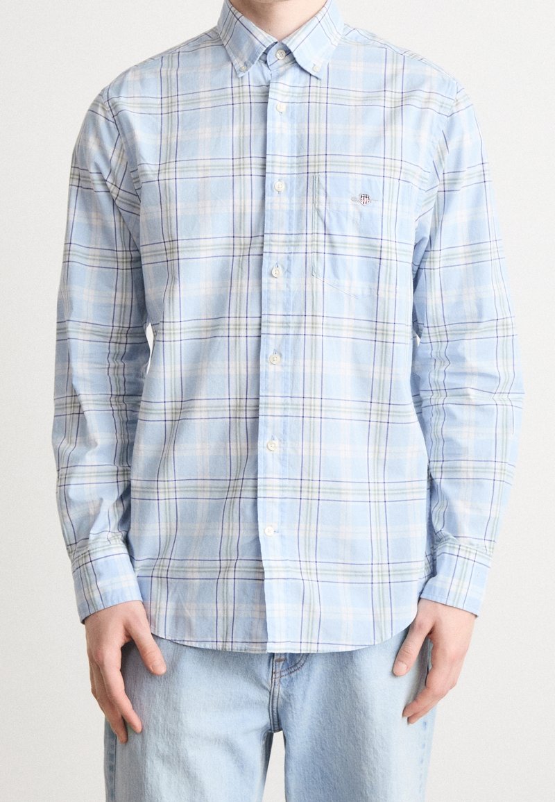 Camicia a quadri blu chiaro realizzata in cotone, con colletto button-down, maniche lunghe e taschino sul petto; presenta strisce bianche e viola.