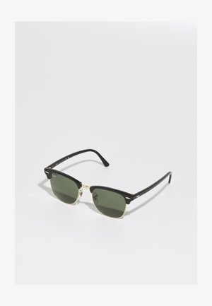 Black and gold sunglasses with green lenses, featuring a cat-eye shape, metallic accents, and a textured frame.