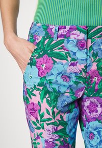 Broek met een bloemenpatroon in levendige roze, groene en blauwe tinten, voorzien van een getailleerde taille en zijzakken. Gemaakt van een gestructureerde stof.