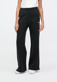 Černé tepláky s volným střihem, elastickým pasem a šňůrkou; mají malý logový detail na straně a měkkou texturu látky.