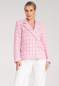 Różowy i biały żakiet w kratę z podwójnym zapięciem, złotymi guzikami, klapami i przednimi kieszeniami. Stylizowany z białymi spodniami.
