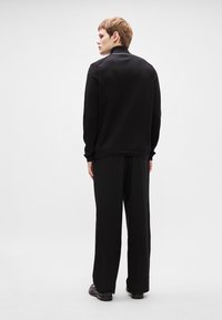 Sweater de malha preta com gola redonda, combinado com calças pretas largas. O conjunto apresenta um caimento descontraído e um design minimalista.