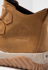 Botte imperméable marron en daim, avec des accents hexagonaux, une semelle en caoutchouc texturée et un logo embossé sur le côté.