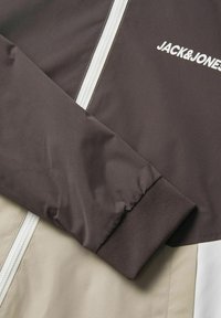Brown and beige bomber jacket with a white zipper and ribbed cuffs. Features the logo "JACK&JONES" in white on the upper left.