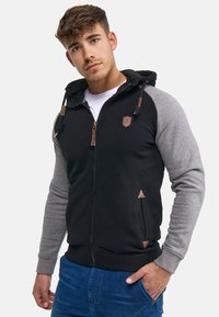 Sudadera con cremallera en negro y gris con un acabado texturizado, capucha con cordón, bolsillos en ángulo y detalles de cuero en la cremallera y los laterales.