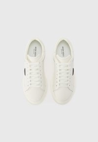 Des baskets blanches en cuir lisse avec un bout arrondi, six œillets et un accent de logo noir sur le côté. Semelle texturée. Lacets plats.