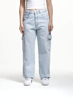 Light blue cargo jeans feature a relaxed fit, multiple side pockets, and a high waist. Worn with white sneakers and a fitted top.