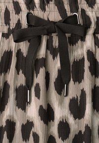 Close-up of beige fabric with black irregular spots and a black tied drawstring threaded through metal eyelets.
