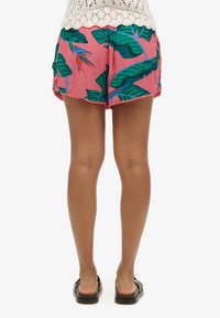 Shorts rosa con stampa di foglie tropicali verdi, con una vestibilità ampia, orlo scallop e tasche laterali. Indossati con sandali neri.