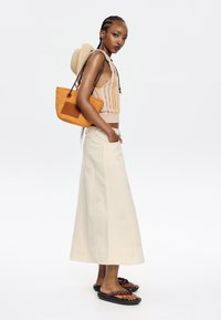 Knit cropped tank with multi-colored stripes, cream A-line skirt with floral embroidery, woven orange bag, and black sandals with braided straps.