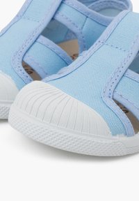 Vaaleansinisiä kangassandaaleja, joissa on valkoiset kumiset varvassuojat ja teksturoidut pohjat. Sisältää ristikkäisiä hihnoja turvallisen istuvuuden ja ilmavien ominaisuuksien takaamiseksi.