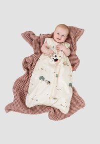 Slaapzak van zacht beige stof met natuurafdrukken, met rits, gelegd op een gestructureerde, blushroze deken met een wafelpatroon.