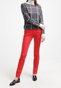 Top gris de manga larga con patrón de cuadrícula blanca combinado con pantalones rojos ajustados. Los zapatos son mocasines negros y brillantes.