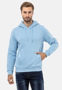 Helles blaues Hoodie mit einer vorderen Tasche, Kapuze mit Kordelzug, gerippten Bündchen und regulärer Passform, kombiniert mit dunklen Jeans.