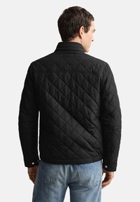 Czarna pikowana kurtka z kołnierzem i mankietami na zatrzaski. Posiada wzór w romby i gładką fakturę, połączona z jasnoniebieskimi jeansami.