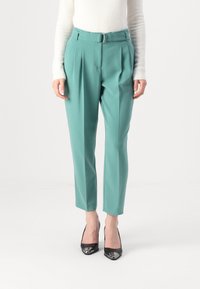 Pantaloni tailored in teal con cintura con cintura, pieghe e gamba affusolata. Abbinati a tacchi a punta nera con dettagli metallici.