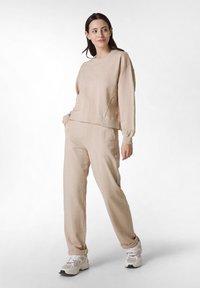 Sudadera beige de gran tamaño con mangas largas y cuello redondo, combinada con pantalones ajustados a juego. El material muestra un acabado suave y texturizado.